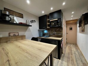 A compact kitchen with a wooden dining table, built-in appliances, and a small island. - 150m from shops, 3rd floor, view mountain, balcony, tv, ski locker, 27m², Les Menuires (Les Menuires)