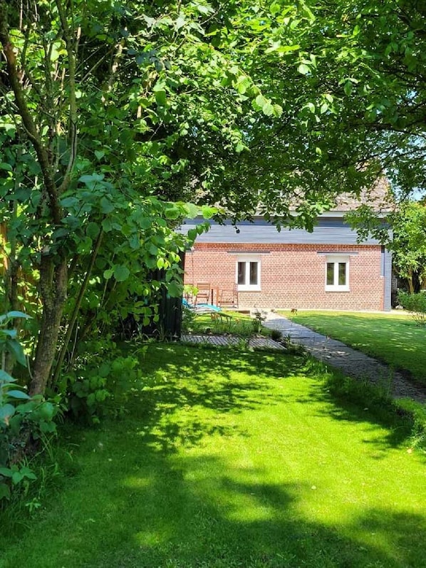 A brick building with a window and a door, surrounded by lush greenery and a well-maintained lawn.