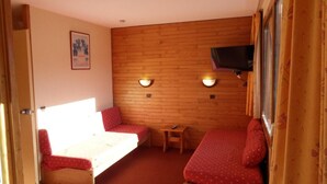 Una habitación pequeña con dos camas, una mesa y dos lámparas en la pared.