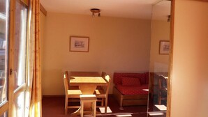 Una habitación con una mesa y sillas de madera, un sofá rojo y dos cuadros en la pared.