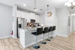 A modern kitchen with a central island, bar stools, stainless steel appliances, and a decorative wall piece. - Make your own Escape to Disney in this fantastic pool townhouse! (Davenport)