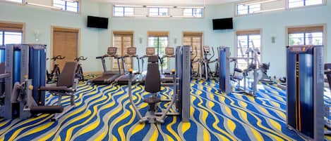 Une salle de sport équipée de machines de cardio, de postes d’entraînement avec poids et d’un tapis à motifs.