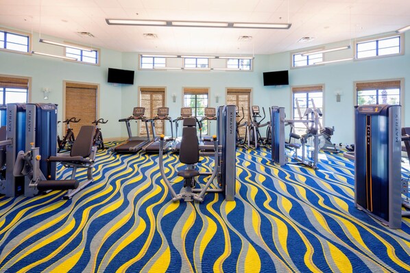 Une salle de sport équipée de machines de cardio, de postes d’entraînement avec poids et d’un tapis à motifs.