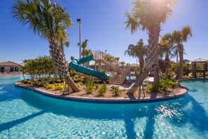Un espace piscine avec un toboggan, des palmiers et un ciel d’un bleu éclatant.