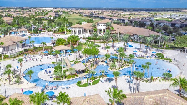 Relax by the central pool surrounded by palm trees and sun loungers, with multiple smaller pools and a water slide nearby.