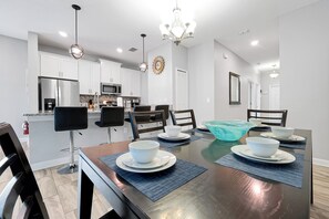 A modern dining room with a dark wooden table, white plates, and blue placemats. - Make your own Escape to Disney in this fantastic pool townhouse! (Davenport)