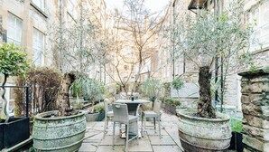 A courtyard with a table and chairs, surrounded by large planters and trees.