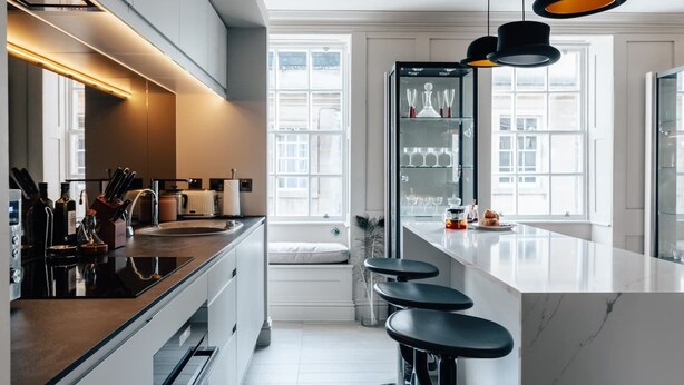 A modern kitchen with a large island, bar stools, and a glass-fronted refrigerator.