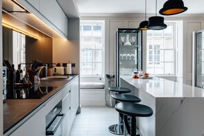 Ett modernt kök med en stor köksö, barstolar och ett kylskåp med glasdörr.