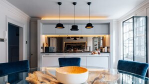 A modern dining area with a glass table, blue chairs, and a central wooden bowl.