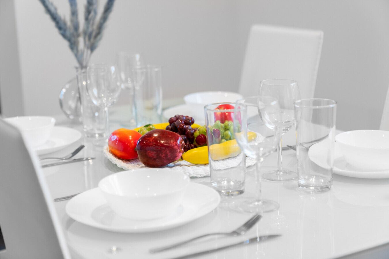 Une table à manger dressée avec des assiettes, des couverts et un arrangement de fruits.