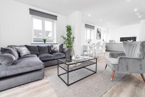 A modern living room with a grey sofa, a glass coffee table, and a grey armchair.