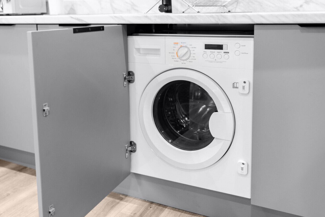 Eine Waschmaschine mit Frontöffnung in einer modernen Küche, mit einem grauen Schranksystem und einer Marmorarbeitsplatte.