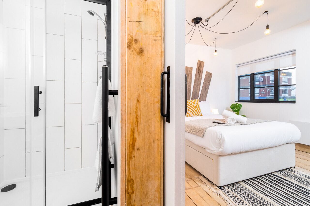 A modern bedroom with a large bed, a wooden door, and a shower area.