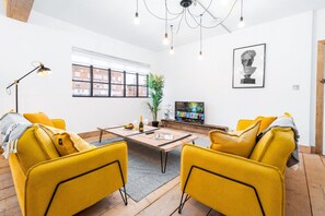 A modern living room with yellow chairs, a wooden coffee table, a potted plant, and a television. - Newtown Lofts - Luxe Apartment - Parking (Birmingham)