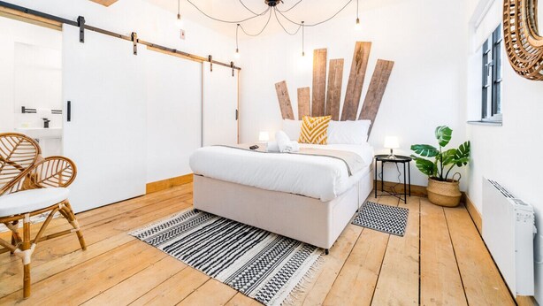 A modern bedroom with a bed, wooden floor, and a ceiling light fixture. - Newtown Lofts - Luxe Apartment - Parking (Birmingham)
