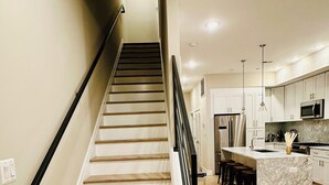 A staircase leading to a kitchen with a marble island, wooden flooring, and modern appliances. - Stunning Private Rooftop Penthouse in DC! Modern Luxury with Breathtaking Views! (Washington)