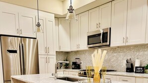 A modern kitchen with white cabinets, a stainless steel refrigerator, a microwave, and a marble island with bar stools. - Stunning Private Rooftop Penthouse in DC! Modern Luxury with Breathtaking Views! (Washington)