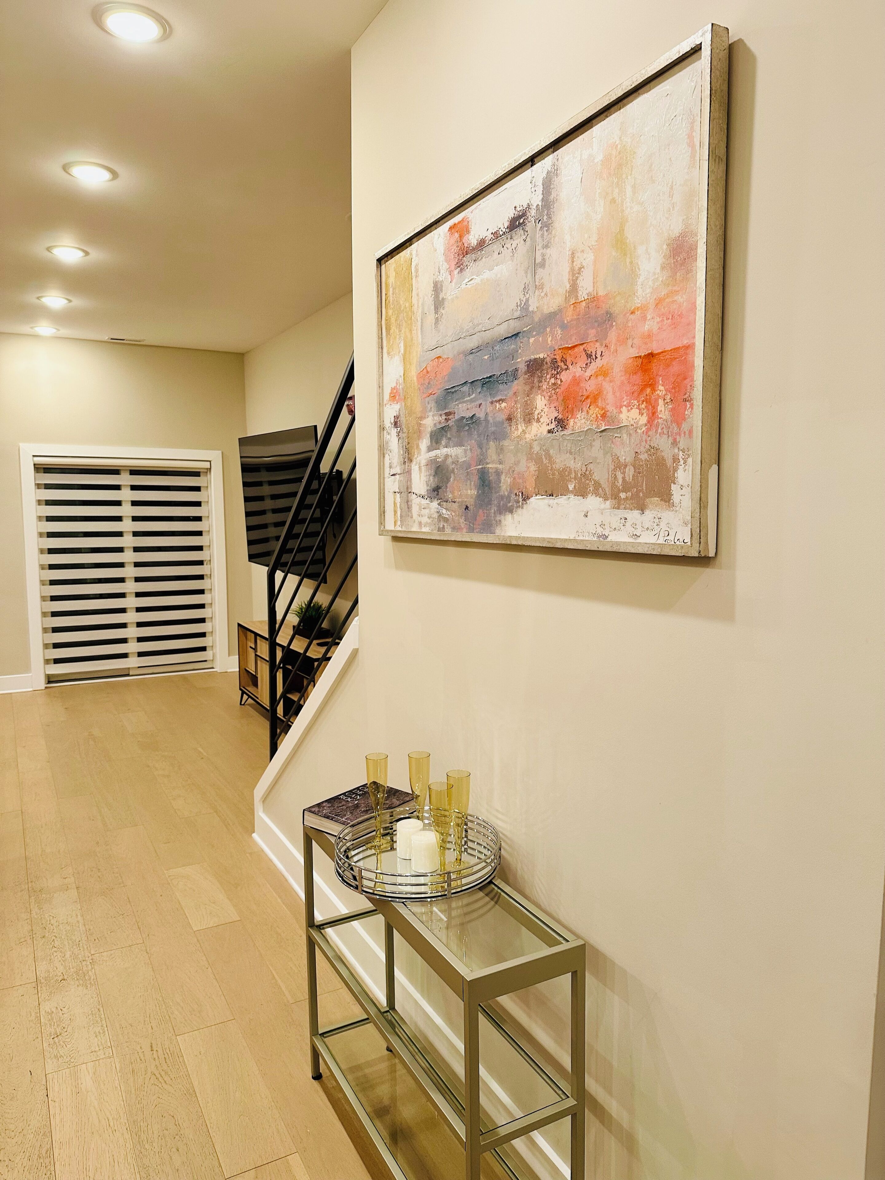 A hallway with a staircase, a glass table with candles, and an abstract painting on the wall.