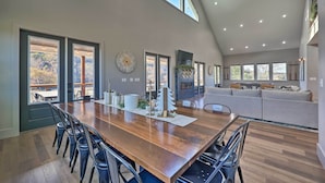A spacious dining area with a long wooden table and chairs, large windows, and a high ceiling with recessed lighting. - Lavish Riverfront Escape w/ Gas Grill! (Glenwood)