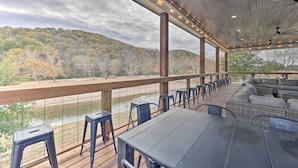 An outdoor patio with tables and chairs, overlooking a river and forested hills. - Lavish Riverfront Escape w/ Gas Grill! (Glenwood)