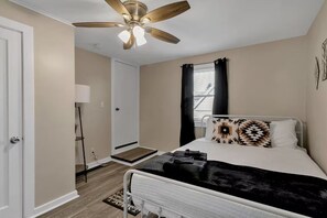 A bedroom with a bed, a ceiling fan, a window with curtains, a bedside table, and a nightstand.