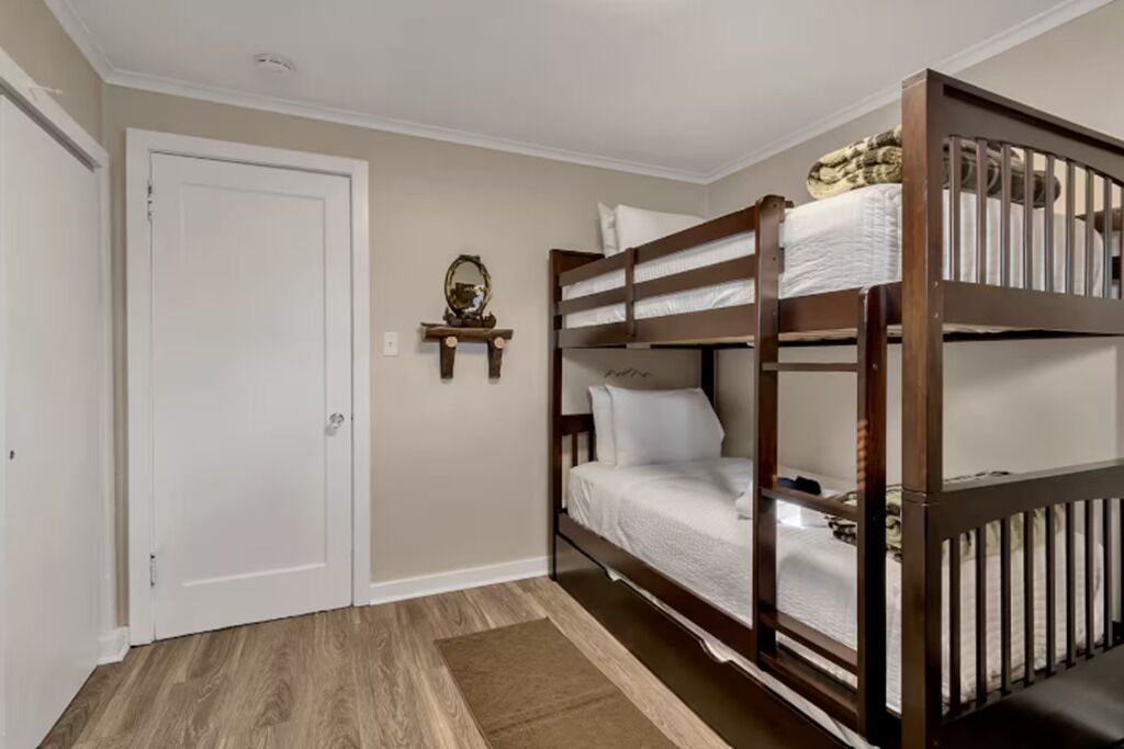 A room with a bunk bed, a white door, a small table with a mirror, and a brown rug.