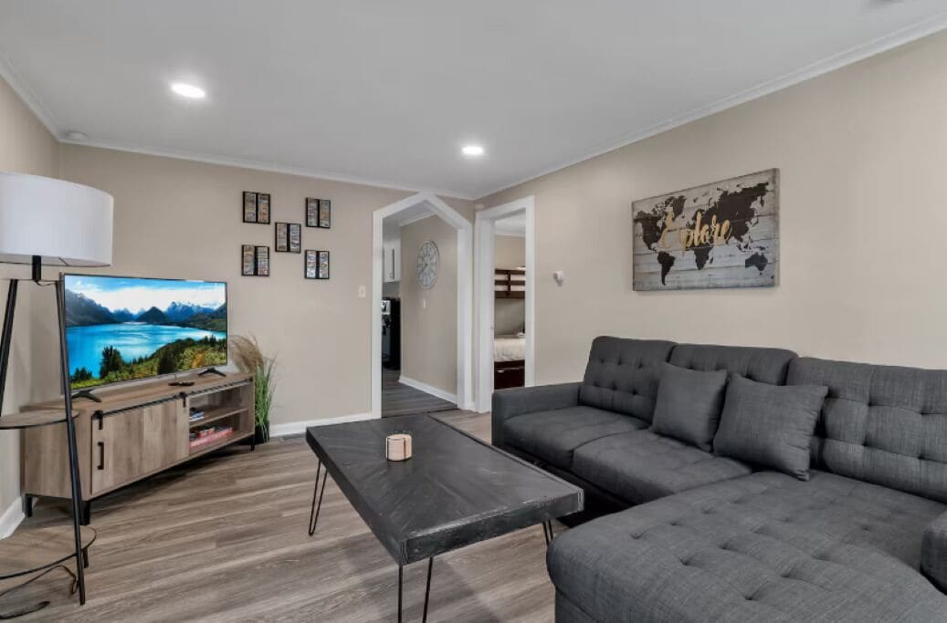 A living room with a grey sofa, a TV on a wooden stand, and a world map artwork on the wall.