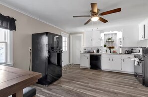 A modern kitchen with white cabinets, a black refrigerator, a ceiling fan, and a dining area with a wooden table.