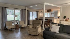 A spacious living room with a grey sofa, beige armchair, and striped chairs. A kitchen is visible in the background. - The Quail's Nest! Convenient to downtown, quiet and fully remodeled! (Thomasville)