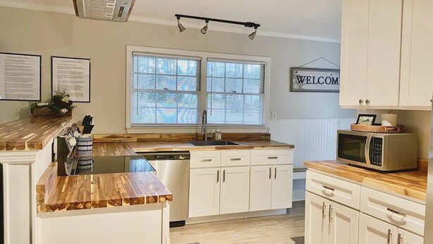 A modern kitchen with white cabinetry, a wooden countertop, a built-in microwave, and a window with blinds. - The Quail's Nest! Convenient to downtown, quiet and fully remodeled! (Thomasville)
