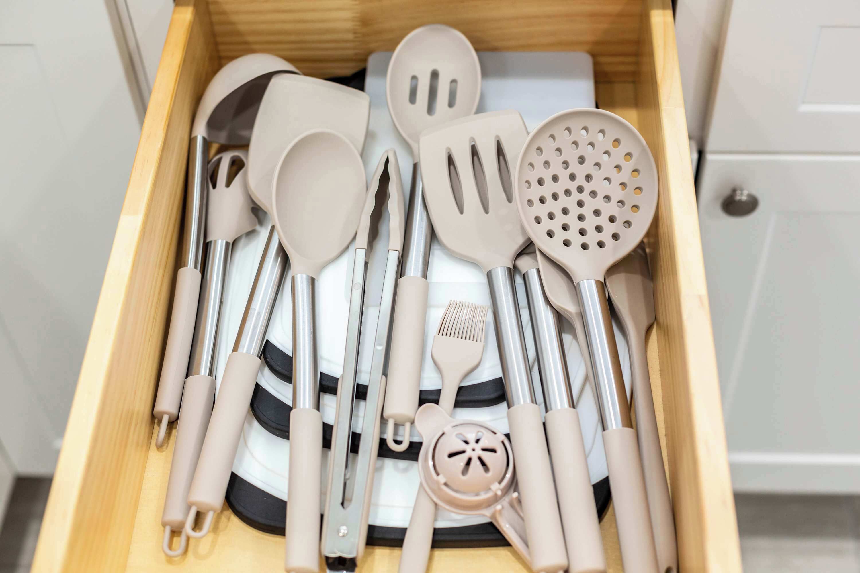 A drawer containing various kitchen utensils including spatulas, a grater, and a strainer.