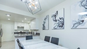 Una cocina moderna con gabinetes blancos, una isla de mármol y obras de arte contemporáneas en las paredes.