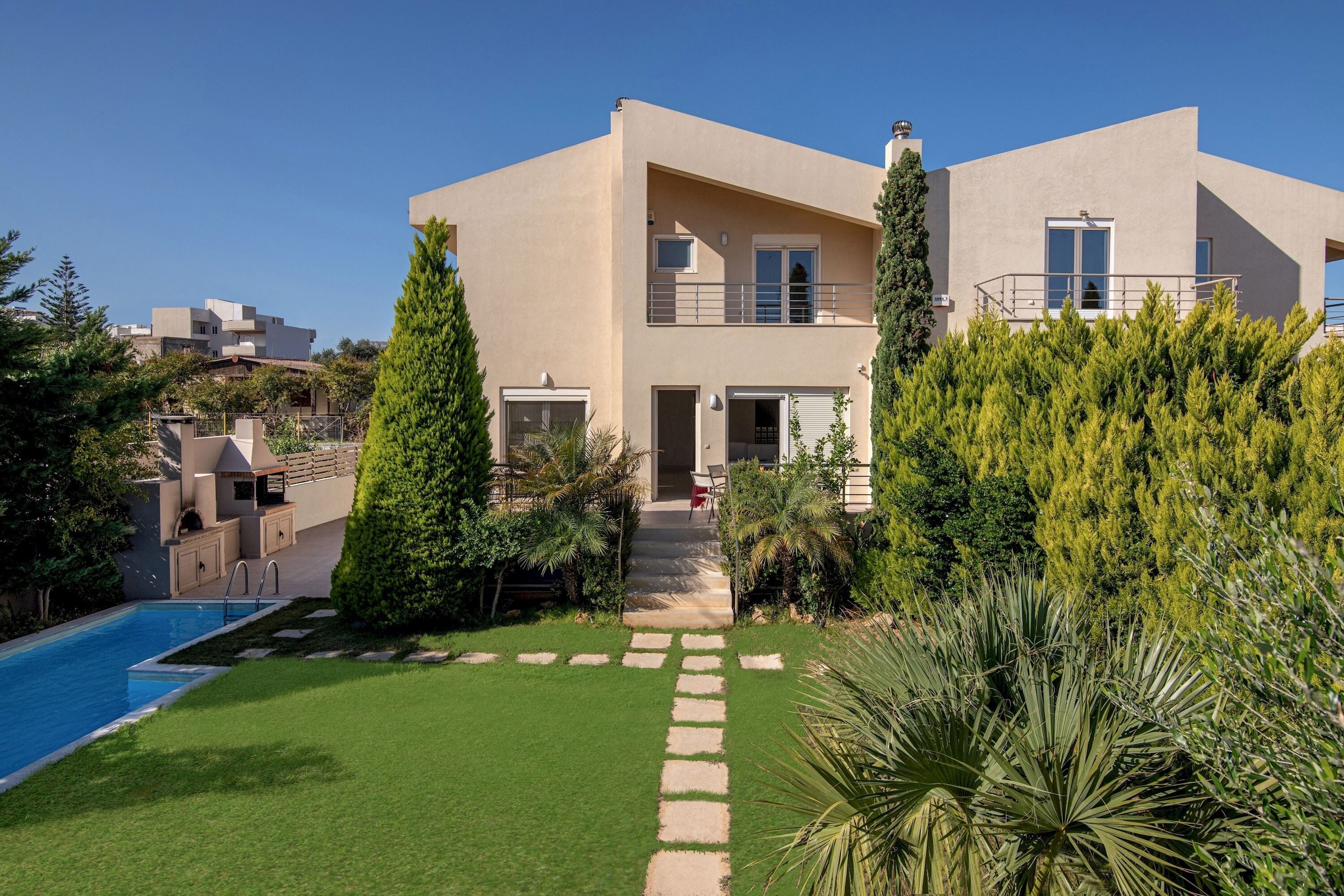 Uma casa moderna de dois andares, com piscina, um jardim bem cuidado e um céu limpo.