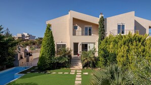 A modern two-story house with a swimming pool, a well-maintained garden, and a clear sky.