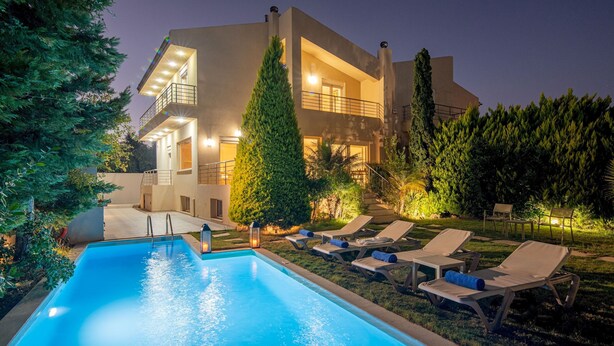 A modern two-story house with a swimming pool, lounge chairs, and a well-lit outdoor area.