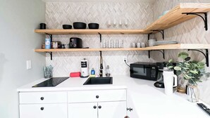 A compact kitchen with white cabinetry, a microwave, a sink, and wooden shelves above.