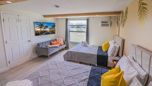 A bedroom with two beds, a sofa, a painting, and a window with a view.