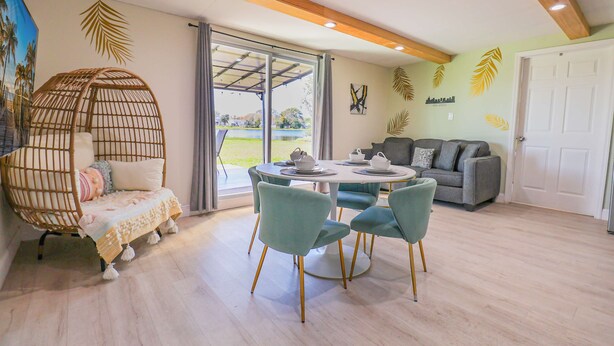 A modern living room with a round table, teal chairs, a grey sofa, and a wicker chair with a cushion.