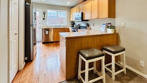A kitchen with wooden cabinets, a central island with stools, stainless steel appliances, and a window with a view. - Boise Avenue Getaway • 3BR/3BA • Yard • Parking for 2 • Near BSU & Downtown • Spacious (Boise)