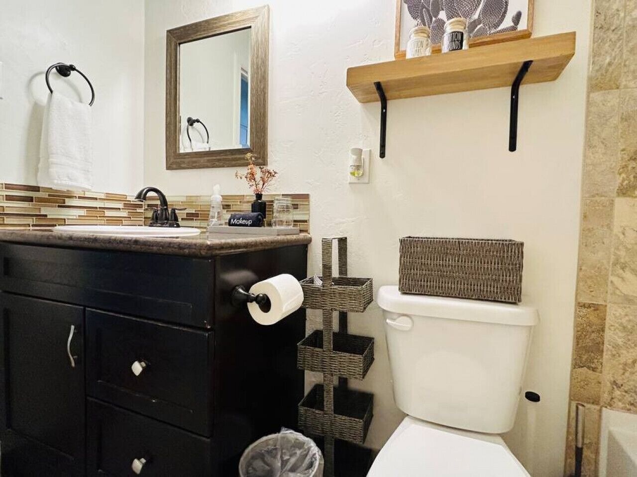 Une salle de bain avec un meuble-lavabo noir, des toilettes, un miroir et une étagère contenant des articles de toilette.