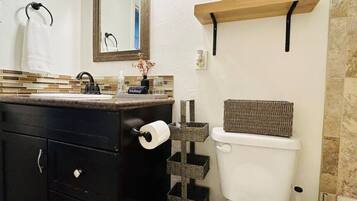 Une salle de bain avec un meuble-lavabo noir, des toilettes, un miroir et une étagère contenant des articles de toilette.