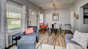 A cozy living room with a grey sofa, a red chair, a dining table with chairs, and a wooden floor. - The Red Bench Cottage | Historic Charm • Fenced Yard • Walk to Hyde Park • Central Boise (Boise)