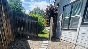 A gravel pathway leading to a wooden fence and a house with a window. - The Red Bench Cottage | Historic Charm • Fenced Yard • Walk to Hyde Park • Central Boise (Boise)