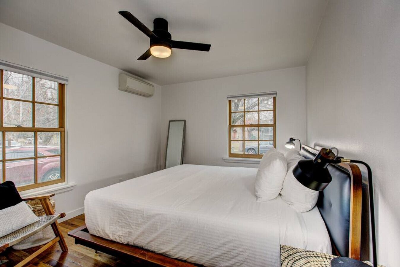 A bedroom with a large bed, a ceiling fan, two windows, a chair, and a lamp.
