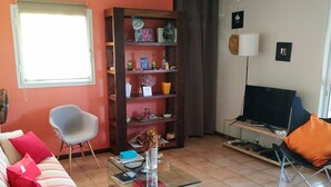 Un soggiorno con divano, tavolino in vetro, libreria, televisore e ventilatore a soffitto.