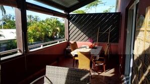 Un balcone coperto con un tavolo e sedie, vista su palme e un muro decorativo.