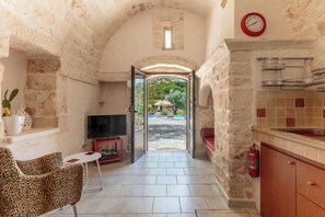 Un estrecho pasillo de paredes de piedra que conduce a un espacio exterior con vistas a vegetación y una piscina.