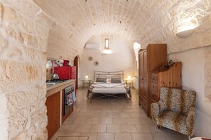 Una habitación pequeña con paredes de piedra, una cama, una mesita y un sillón estampado con diseño de leopardo.