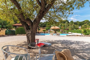 A pool area with a table and chairs, a tree, and a view of the surrounding landscape.